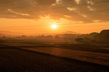 冬の田園地帯に昇る朝日とオレンジ色の空・日本の12月の早朝風景

