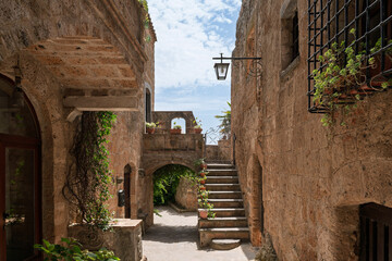Italy - Bagnoregio - Civita di Bagnoregio - Shaded courtyard passage with exterior stair, arched tunnel and lantern between warm tuff walls
