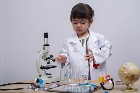 Cute little girl wearing a lab coat playing scientist with microscope and test tubes. Concept of early education, STEM learning, curiosity, creativity, and children imagination in science. - Powered by Adobe