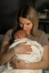 Mom gently holds her wrapped baby in a cozy indoor setting during the evening hours
