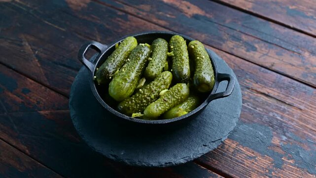 Pickles in a black dish on a wooden table with a rustic background and natural light showing details of the pickles