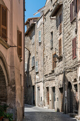 Obraz premium Italy - Viterbo - Historic center - Narrow cobbled street with stone facades, shutters and archway shadow