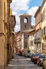 Naklejka premium Italy - Viterbo - Pianoscarano - Cobblestone street with colorful houses and bell tower in background