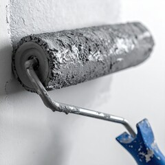 Close-up of a paint roller coated in gray paint, attached to a metal handle, against a light gray wall