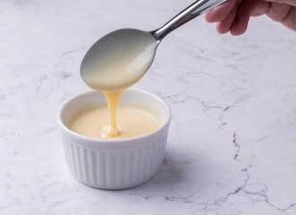 Hand pouring condensed milk in a bowl over marble background