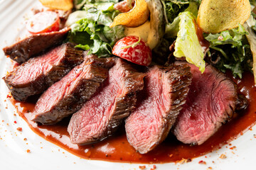sliced rare steak pieces with a rich red sauce, served alongside a crisp green salad topped with potato chips and cherry tomatoes on a white plate.