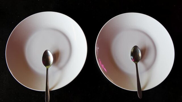 empty plates with spoons on black background depicting minimalist dining concept