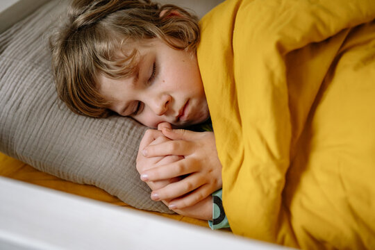 Child sleeps under yellow blanket in cozy bed during daytime