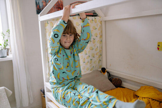 Child plays on bed frame while wearing banana pajamas in a cozy room