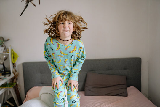 Child jumps on bed while wearing pajamas decorated with bananas in a bedroom