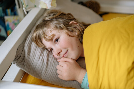 Child resting in bed with yellow blanket and soft pillow during morning hours
