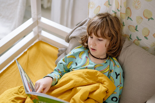 Boy reads book in bedroom while wearing pajamas and sitting on bed