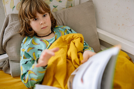 Boy reads a book while sitting in bed wearing pajamas in a cozy bedroom
