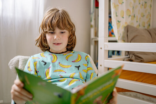 Boy reading a book in pajamas in his bedroom during the morning hours