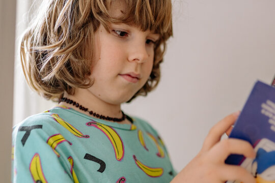 Boy reading a book while wearing pajamas in a bedroom during morning hours