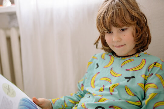 Boy reading a book in bedroom while wearing pajamas with banana print