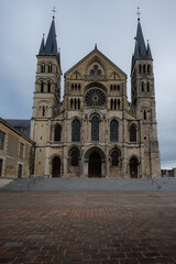 Fototapeta premium Frontal view of Basilique Saint-Remi in Reims under a clouded sky, highlighting its Gothic façade, stone towers, and historic architectural details.