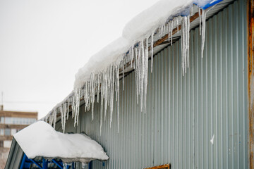 icicles made of ice hang on the snow-covered roof of a house