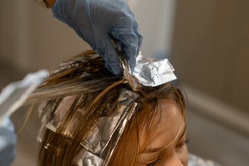 Hair coloring process in a modern salon with highlights using foils on a clients blonde hair