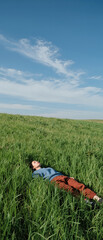Young man relaxes in grassy field under blue sky