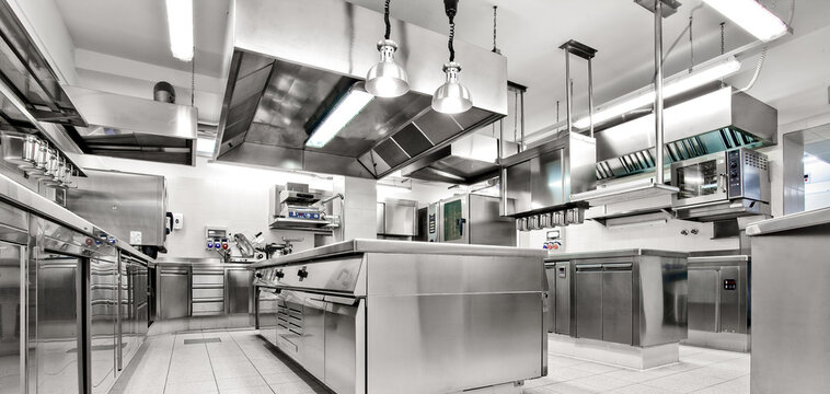 Spacious commercial kitchen with ovens, stoves, prep counters, and ventilation hoods&mdash;ideal for high-volume culinary operations.