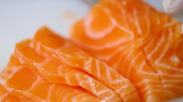 Close-up footage of a chef slicing fresh raw salmon fillet for sashimi or sushi preparation. Professional food preparation process with clean cuts, vibrant texture,  Ideal for Japanese cuisine.