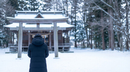雪の神社の鳥居前に立つ日本人女性の後ろ姿、冬の参拝風景