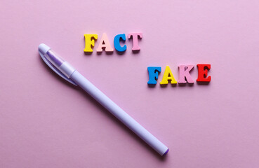 Words fact and fake with pen on purple background.