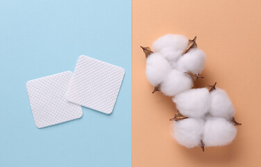 Square cosmetic pads for makeup removal and cotton flowers on blue pink background. Beauty concept....