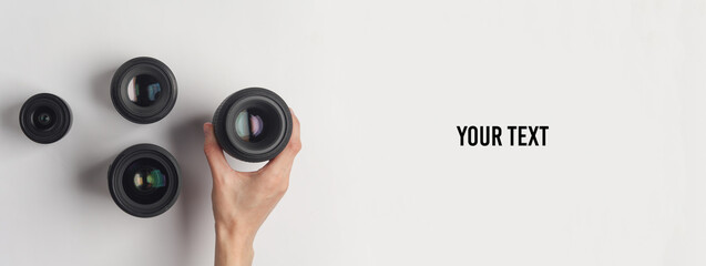 Hand holds professional camera lens on white background with copy space. Top view