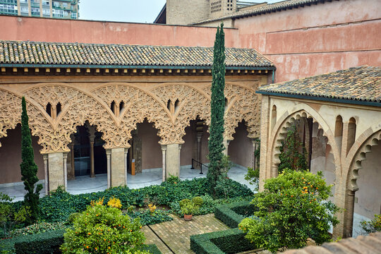 Carved arches surround a lush courtyard inside Palacio de la Aljafer&iacute;a in Zaragoza, Espa&ntilde;a, where trimmed gardens and stone columns shape a slow cultural walk, harmony