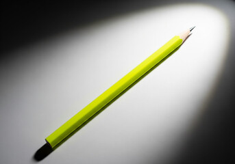 Sharp yellow pencil lying on a white surface under a dramatic spotlight - with copy space.