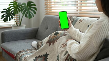 Person holding a smartphone with a green screen on a couch with a blanket