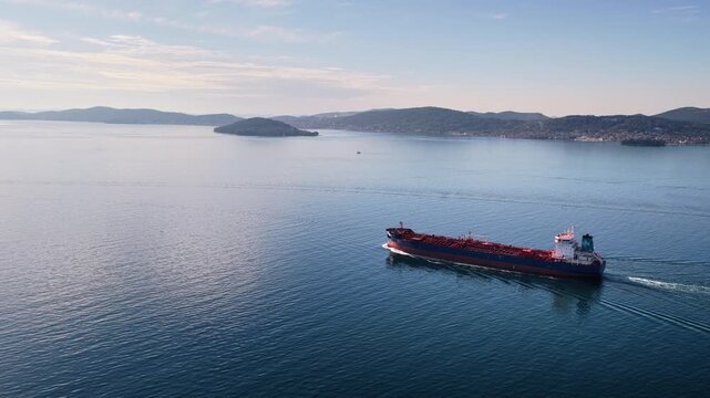 Aerial drone view of an oil tanker traveling across open Adriatic waters with distant mountain ridges and coastal towns visible on the horizon