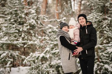 Father, mother hugging child, walking in winter park. Dad, mom embrace daughter, enjoying snowy forest and snowfall. Portrait kid hugs parents having fun. Frosty winter season. Happy family holidays.