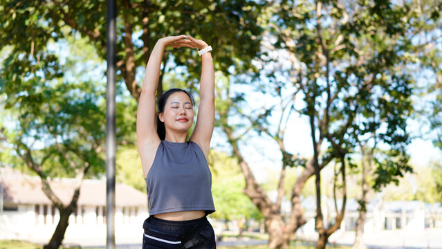Healthy young Asian runner woman warm up the body stretching before exercise at park under warm light morning. Lifestyle fitness and active women exercise in urban city concept.