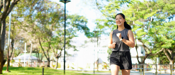 Young smiling sporty woman running in park in the morning. Fitness girl jogging in park