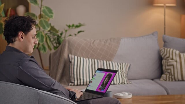 Smiling young man sitting in chair and looking at laptops screen while examining profiles and bios of different women