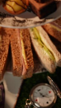 A plate of sandwiches and a clock with the hands on the number 3 and 9. The sandwiches are cut in half and arranged on a plate