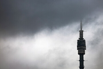 Fototapeta premium Moscow, Russia - October 28, 2025: Ostankino TV tower against a backdrop of dark clouds. Ostankino TV Tower in the fog. image of a TV tower with space for an inscription