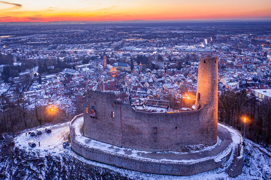 Aerial view of medieval Windeck castle ruin atop a snow-dusted hill, its stone walls illuminated against the twilight sky, Weinheim, Baden-Wurttemberg, Germany.