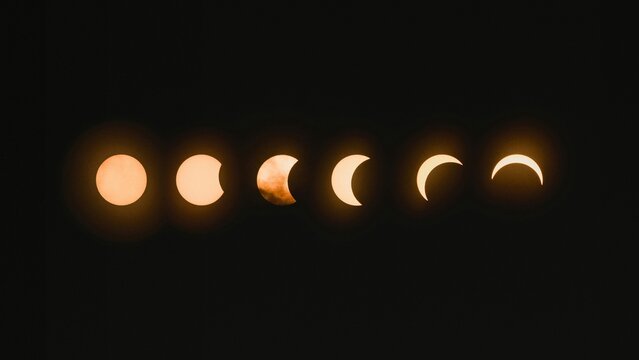 A series of sun eclipse phases shown as glowing orange crescents and circles against a dark black background illustrating the progression of an astronomical event.