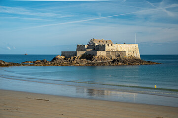 The Fort du Petit B&eacute; near Saint-Malo, France, a historic tidal island fortification, photographed under a clear blue sky, showcasing stone ramparts and coastal military architecture.

