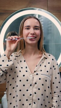 Teenage girl with braces brush teeth looks at the camera and shows a like in the morning at home. Slow motion.