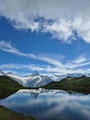 Fototapeta premium Stunning reflection of snowy alpine mountain in a calm lake under blue sky with clouds in Switzerland