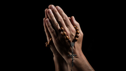 Close up of praying hands holding a wooden rosary with crucifix. Religious Christian faith concept on black background with copy space