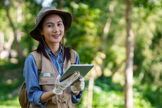 Asian adult woman botanist conducts plant research in natural forest environment using digital tablet for data collection and scientific analysis