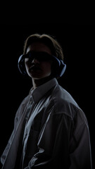 Fototapeta premium Person wearing headphones and visor in dark studio light. Concept of technology branding, cyber style editorials, electronic music culture, fashion promo, futuristic identity visuals.