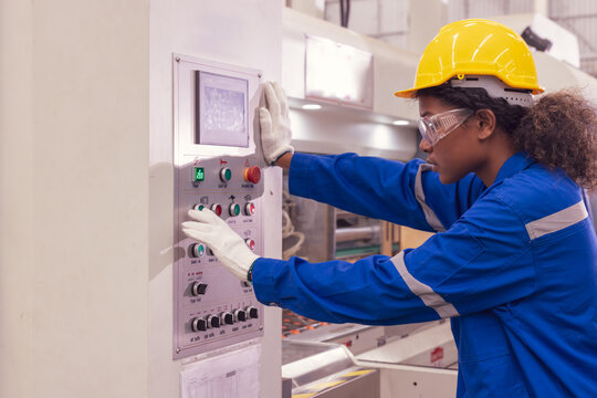 Female african american worker in blue jumpsuit and yellow hardhat operating the machine. Paper factory manufacture.