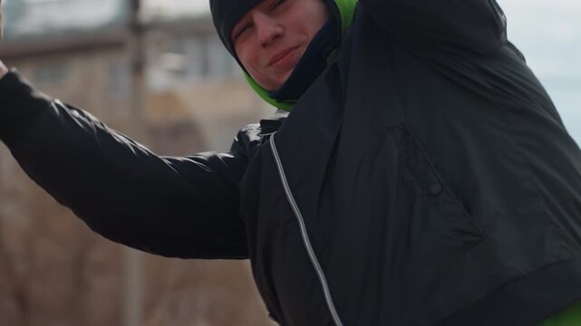 young caucasian goalkeeper reaching to catch ball with arms extended, beanie and dark jacket, focused expression and urban apartment backdrop, close-up motion showing reflex and training intensity